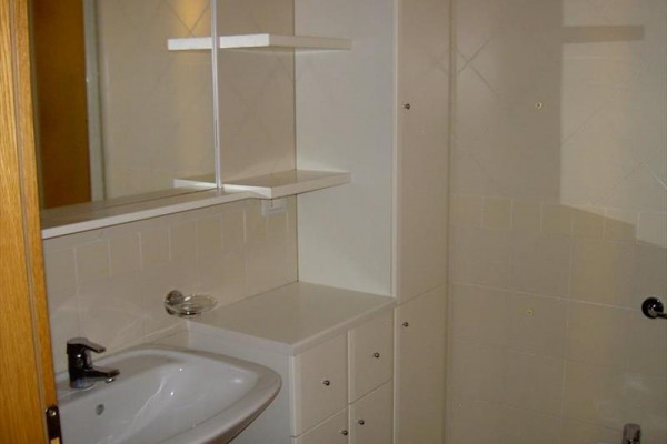 Umyvadlo se zrcadlem a skříňkami v malé koupelně s bílými dlaždicemi.  