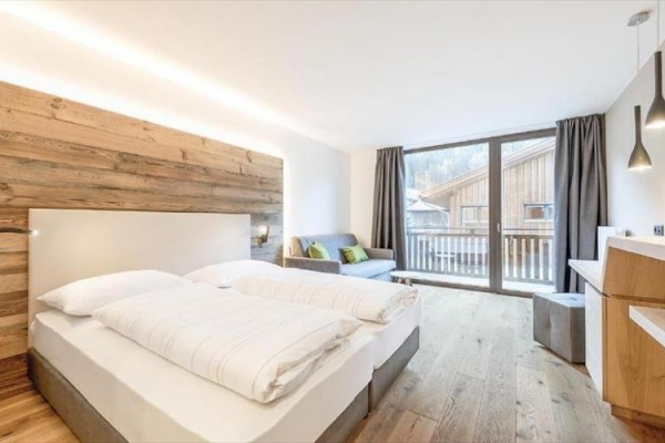 Moderní hotelový pokoj s manželskou postelí, pohovkou a výhledem na balkon.