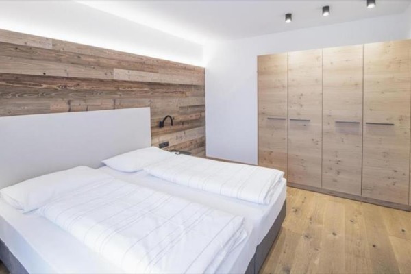 Moderní ložnice s dřevěnou podlahou, postelí a vestavěnou skříní.