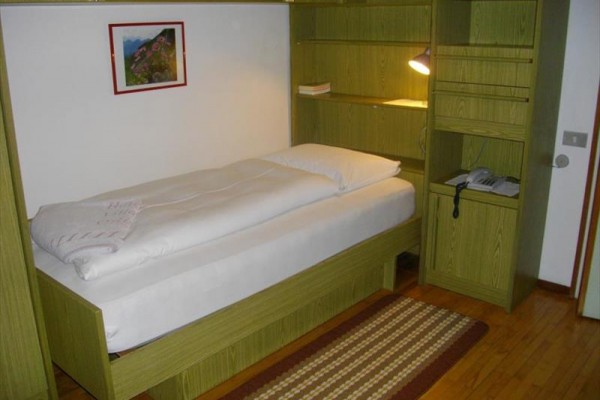 Jednolůžková postel v pokoji s dřevěným nábytkem a koberčkem.