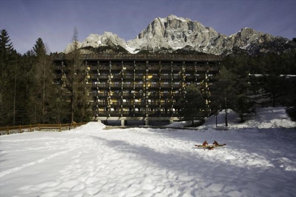 Velký hotel obklopený sněhem a horami na pozadí.