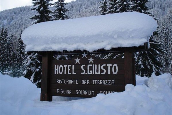 Dřevěná cedule hotelu S. Giusto pokrytá sněhem v zimní krajině.