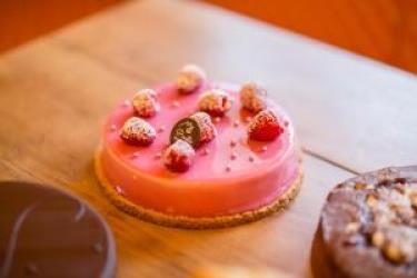 Kulatý růžový dortík zdobený malinami a cukrem.