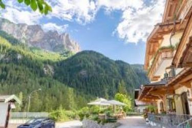 Hotel s balkonem v horské krajině s borovicemi a modrou oblohou.