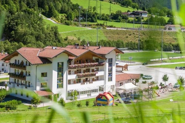 Budova hotelu obklopená zelenou krajinou s lesy a hřištěm.