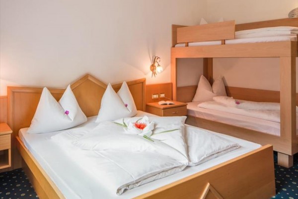 Hotelový pokoj s manželskou postelí a palandou, povlečení zdobeno květinami.