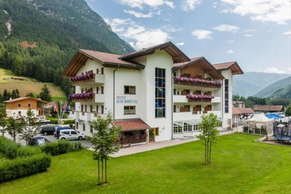 Bílý hotel v horské krajině se zahradou a parkovištěm.
