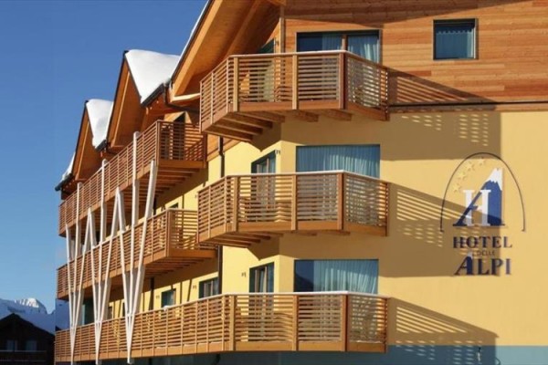 Hotel s dřevěnými balkóny a logem na žluté fasádě.