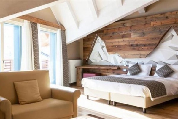 Moderní ložnice s dřevěným obložením na stěně a výhledem na balkon.