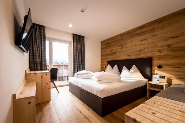 Moderní hotelový pokoj s dřevěným nábytkem, manželskou postelí a balkonem s výhledem ven.