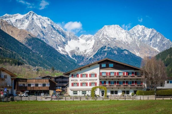 Hotel v horské krajině s zasněženými vrcholky v pozadí.  