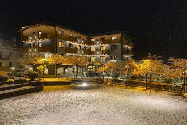 Noční zasněžená budova hotelu s osvětlenými stromy a fontánou.