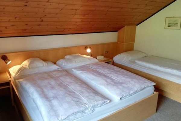 Tři postele v podkrovní ložnici se dřevěným stropem.