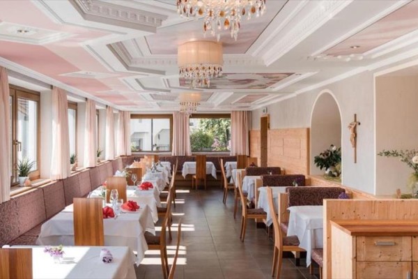Elegantní jídelna s dřevěnými stoly a židlemi, s bílými ubrusy a růžovými květy.  