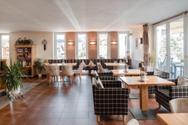 Prostorná restaurace s dřevěným nábytkem a velkými okny.