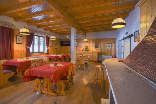 Interiér dřevěné restaurace s červenými ubrusy a dřevěným nábytkem.