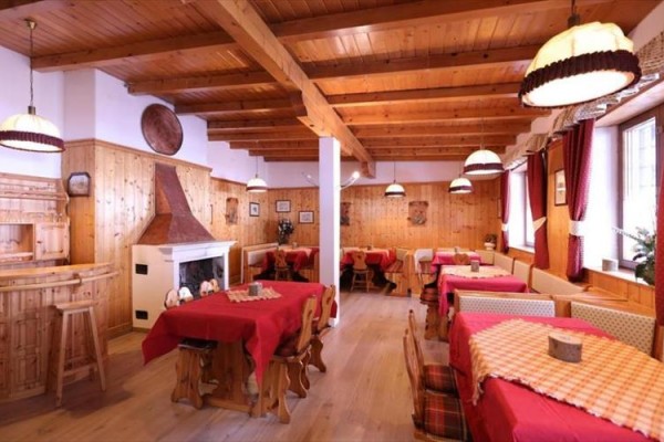 Interiér dřevem obložené restaurace s krbem a červenými ubrusy.