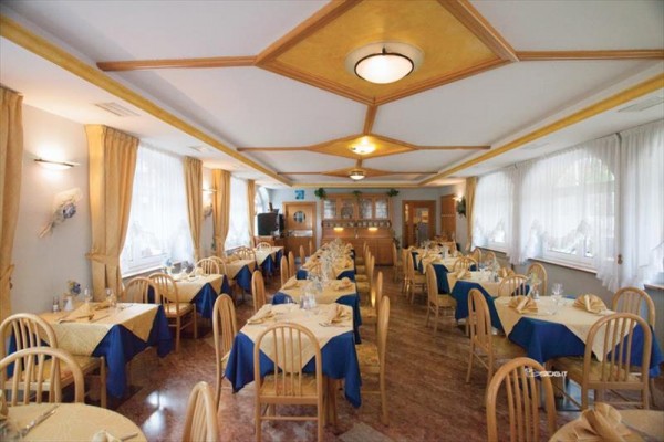 Restaurace s prostřenými stoly a dřevěnými židlemi, vyzdobená modro-žlutými ubrusy.