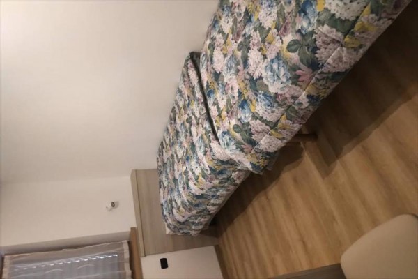 Jednolůžko s vzorovaným přehozem v místnosti s dřevěnou podlahou.