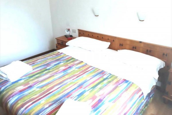 Dvoulůžková postel s barevným přehozem a dřevěným čelem.