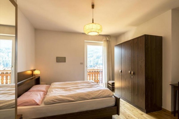 Ložnice s dvojlůžkem, skříní a balkonem s výhledem na les.