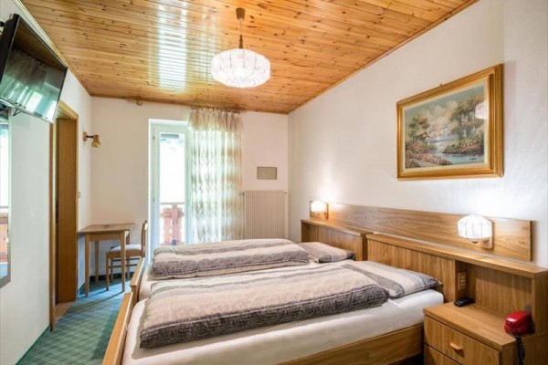 Pokoj s dřevěným stropem, manželskou postelí, televizí a výhledem na balkon.