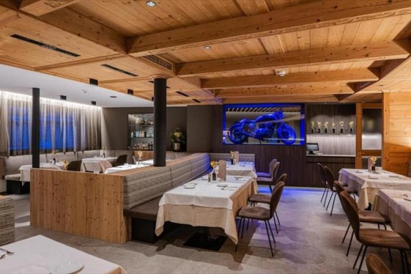 Stylová restaurace s dřevěným interiérem a vystaveným motocyklem v modrém osvětlení.