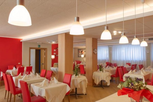 Moderní restaurace s červenými židlemi a bílými ubrusy.