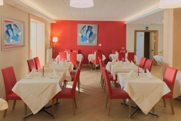 Restaurace s červenými židlemi a bílými ubrusy na stolech.