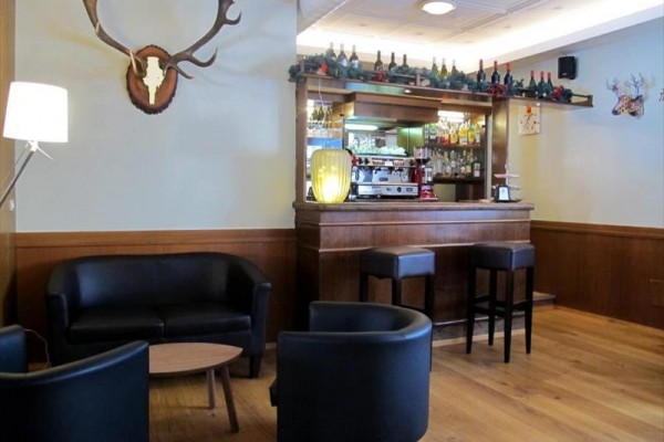 Stylový bar se sedačkami a barovými židlemi, vyzdobený lahvemi a parožím.