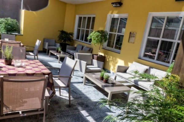 Zahradní terasa s dřevěným nábytkem a rostlinami obklopená žlutými zdmi.  