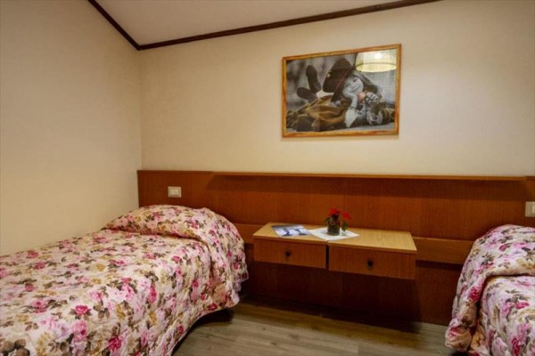Pokoj se dvěma samostatnými postelemi s květinovými přehozy, nočním stolkem a obrázkem na zdi.