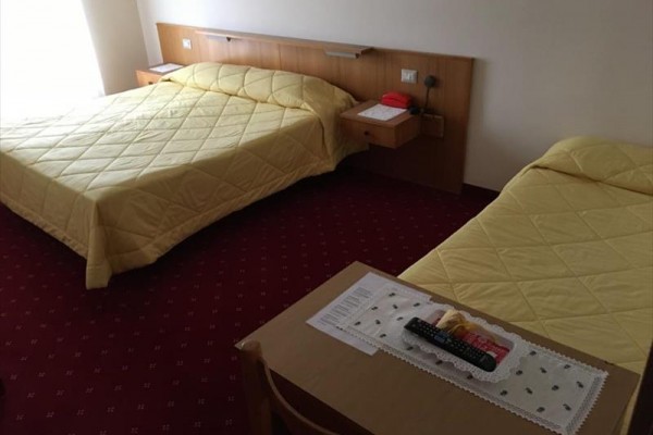 Dva jednolůžkové postele s žlutými přehozy v hotelovém pokoji s červeným kobercem.