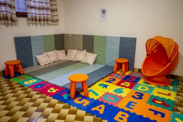 Dětský koutek s polštáři, barevnými podložkami a oranžovými plastovými sedačkami.
