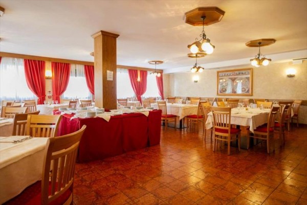 Restaurace s dřevěnými židlemi, bílými ubrusy a červenými závěsy.