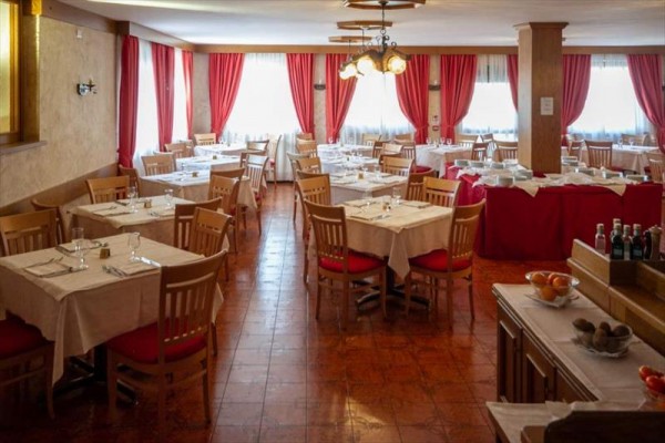 Interiér restaurace s dřevěnými stoly, židlemi a červenými závěsy.