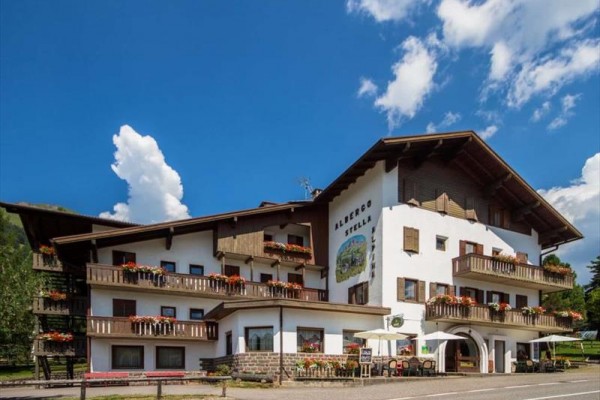 Hotel s dřevěnými balkony a květinovými dekoracemi pod modrým nebem.