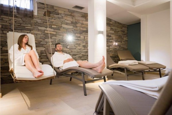 Dva lidé relaxují v županech na lehátkách v místnosti s kamennou zdí.