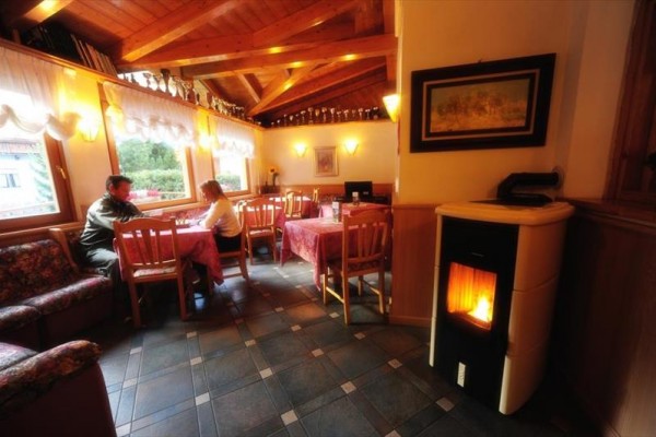 Útulná restaurace s dřevěným stropem, krbem a dvěma lidmi sedícími u stolu u okna.
