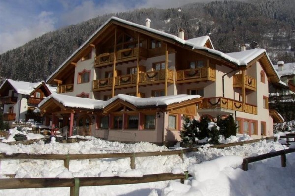 Horský hotel se zasněženou střechou a okolím obklopený lesem.