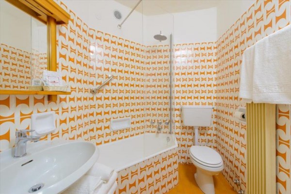 Koupelna s retro oranžovými vzorovanými obklady, vanou a závěsným záchodem.