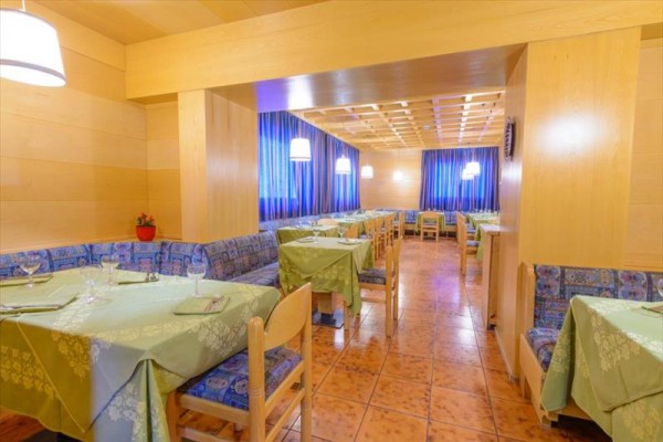 Restaurace s dřevěnými stěnami, modrými závěsy a zelenými ubrusy na stolech.