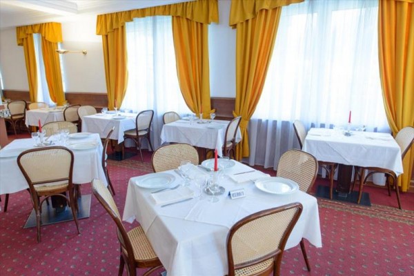 Restaurace s bílými ubrusy a žlutými závěsy.  