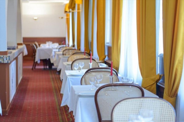 Restaurace s řadami bílých stolů s červenými svíčkami a žlutými závěsy.