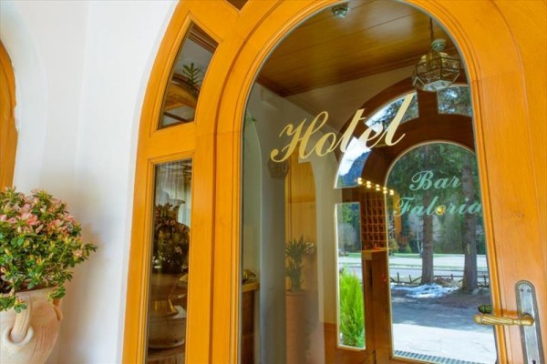 Skleněné dveře s nápisy „Hotel“ a „Bar Faloria“ vedoucí do interiéru budovy s klenutými dveřmi.