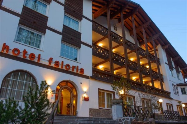 Fasáda hotelu Faloria s dřevěným balkonem a osvícenými okny za soumraku.