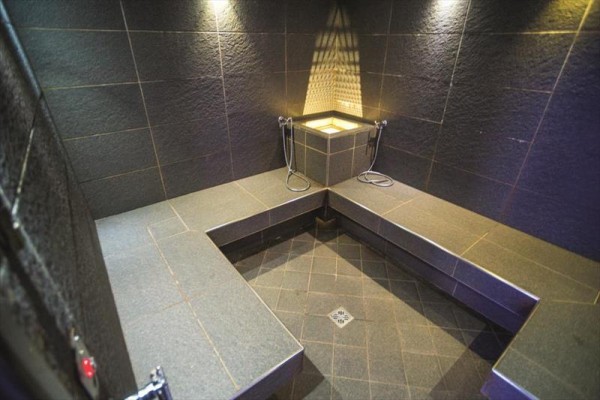 Parní sauna s tmavým obkladem a kamennými lavicemi.