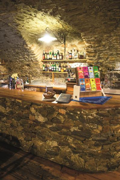 Kamenný bar s lahvemi alkoholu a kávovarem v rustikálním sklepení.  