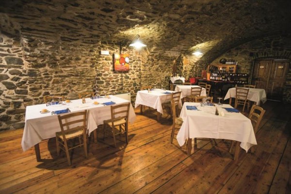 Restaurace s kamennými zdmi, dřevěnou podlahou a několika stolky s bílými ubrusy.