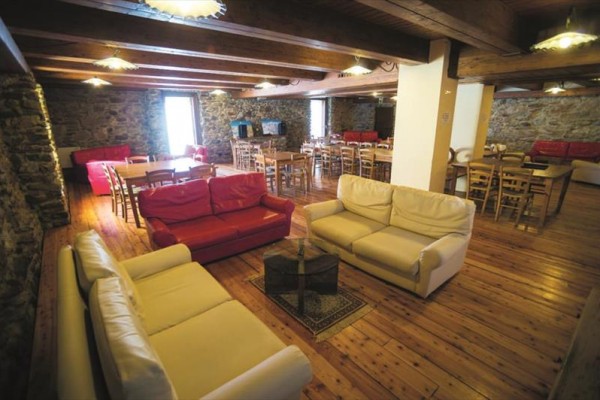 Prostorná místnost s dřevěnou podlahou, kamennými zdmi, sedačkami a stoly.